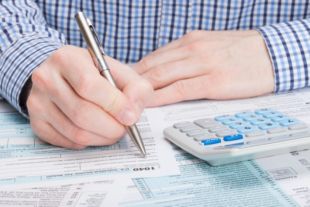 Calculator and IRS Form 1040 on a desk with a hand holding a pen, representing professional tax preparation and filing services